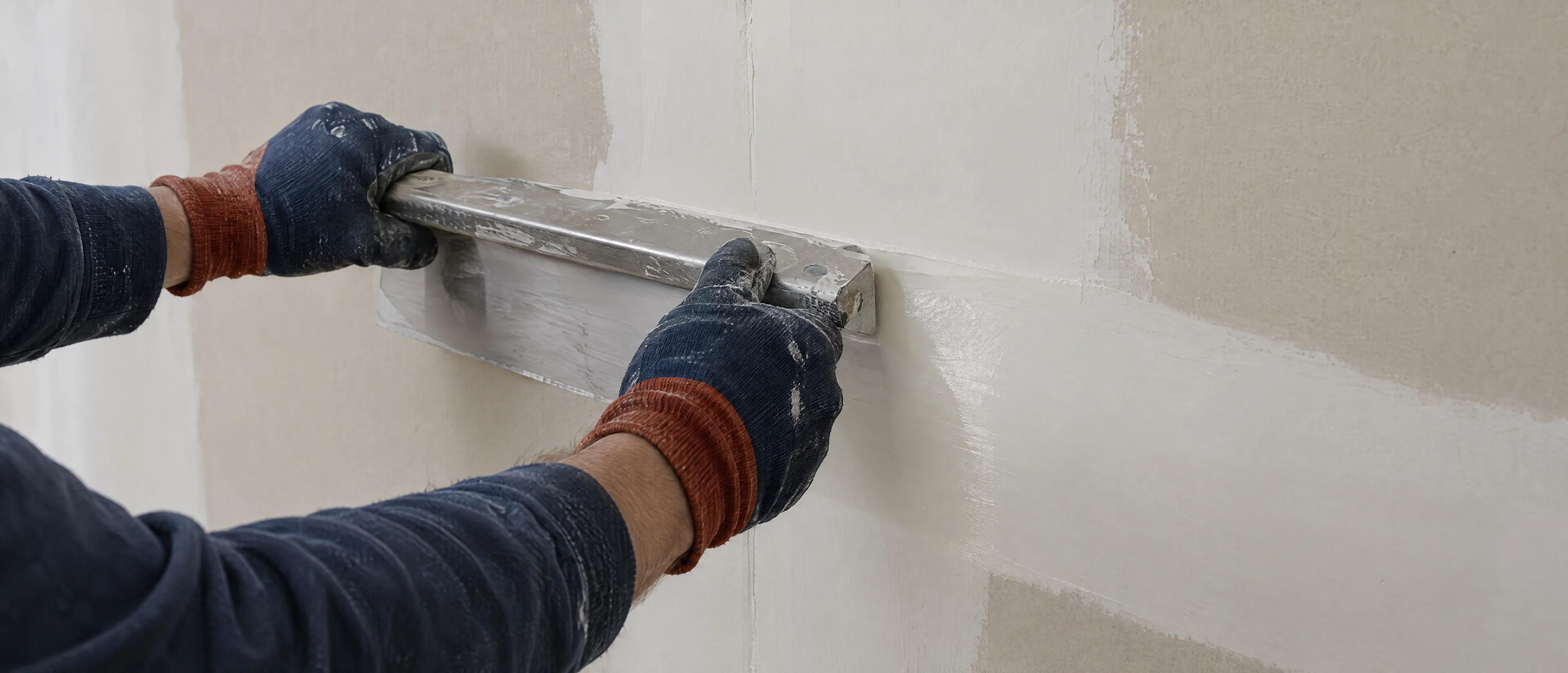 Hände spachteln eine Gipskartonwand glatt