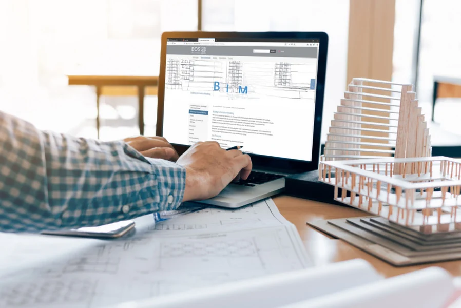 Architekt am Laptop mit BIM-Modell und Gebäudemodell