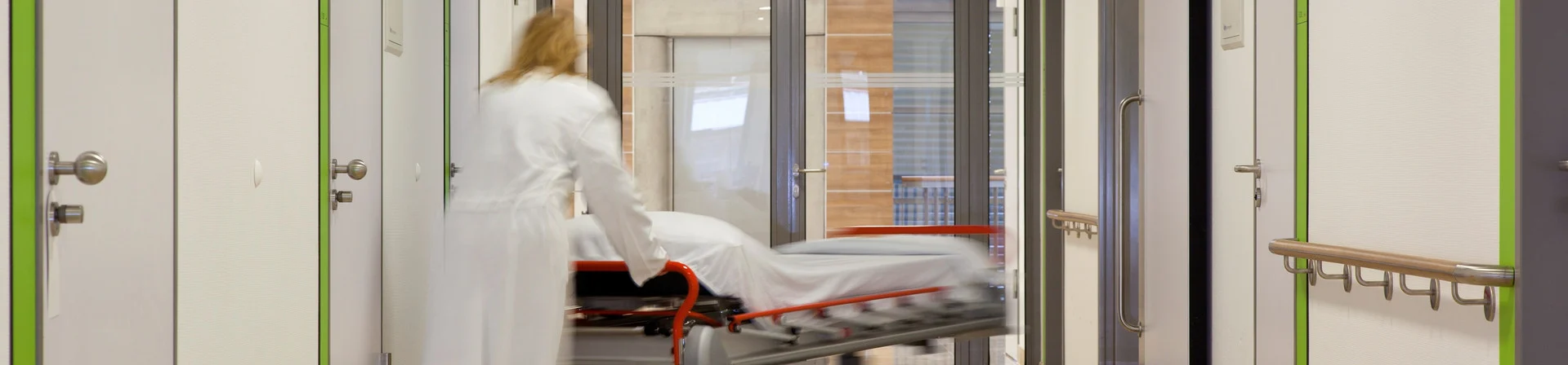 Klinikflur mit Krankenbett vor einer breiten Tür